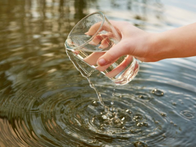 A hand lifts a glass of clean water from a lake.