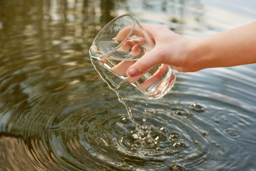 A hand lifts a glass of clean water from a lake.